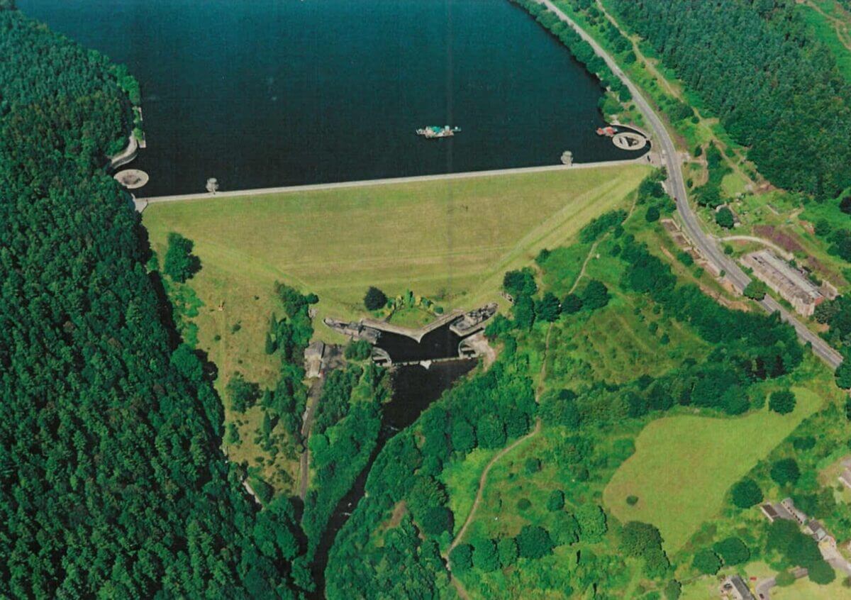 An aerial shot of a dam, surround by green fields and forest
