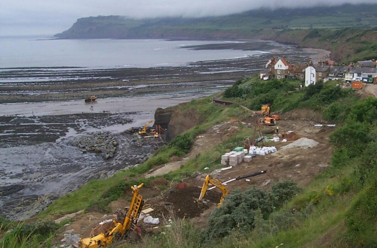 Construction machines and workers reinforcing a cliff against landslides
